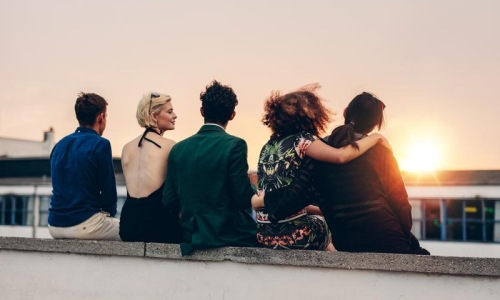 a group of people sitting on a ledge looking at the sun